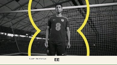 A soccer player in uniform stands in front of a goal net with a yellow graphic line in an indoor setting.