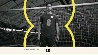A soccer player in uniform stands in front of a goal net with a yellow graphic line in an indoor setting. 