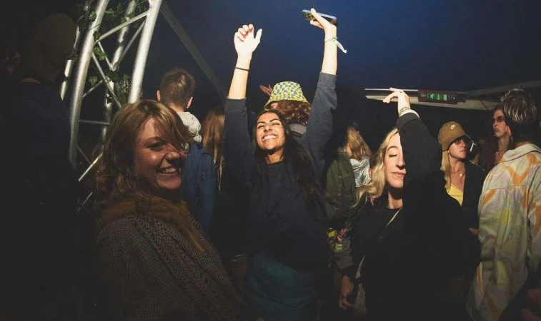Enthusiastic group of diverse adults joyfully dancing indoors at a nighttime social event with vibrant colors and dynamic energy.