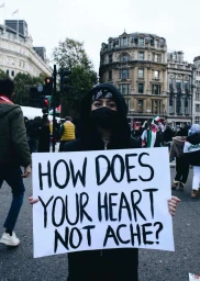 Protester holding a sign reading how does your heart not ache in a London street by Yushy Pachnanda