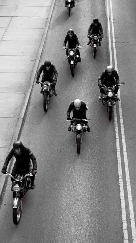 High-angle shot of a group of motorcycle riders on a road with double white lines, showcasing dynamic movement and vintage style.