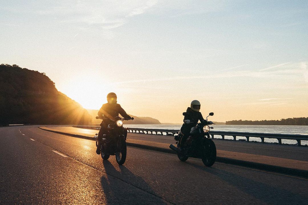 Two motorcyclists riding on an open road at sunset, silhouetted against a bright sky, showcasing adventure and freedom on the road.