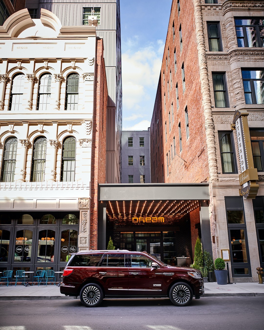 Maroon Lincoln Navigator parked in front of the Dream Hotel, surrounded by brick buildings on a sunny city street.