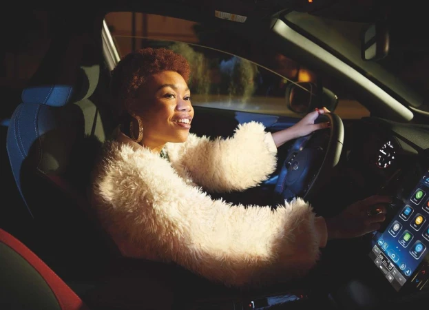 Smiling woman drives a car at night, illuminated by the car's interior lights, focusing on her cheerful expression and modern dashboard.