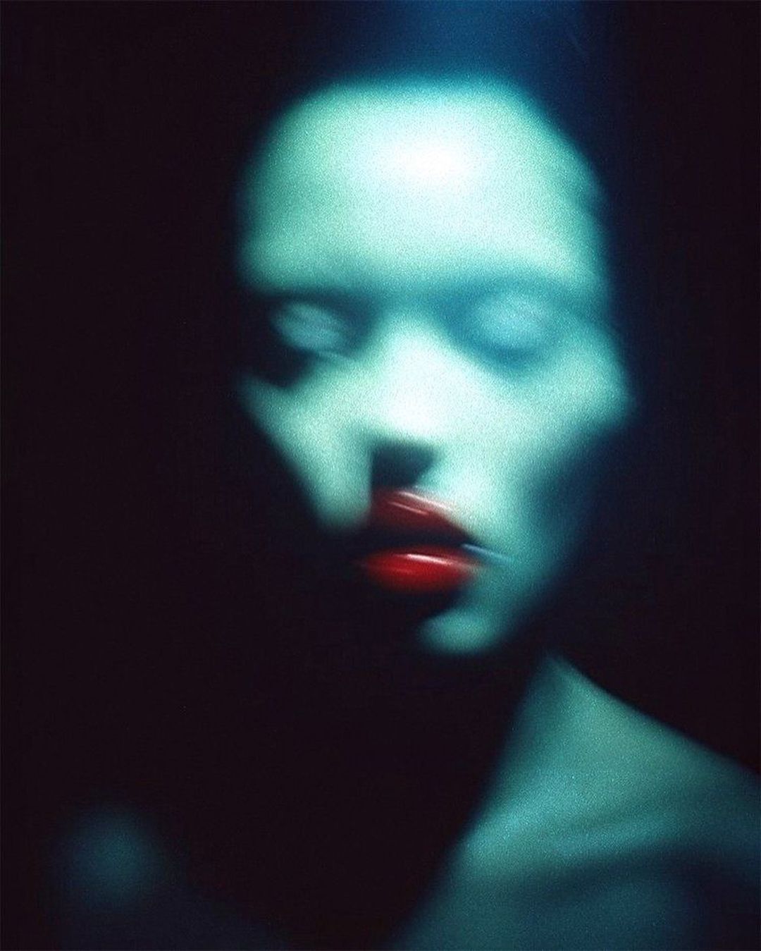 Abstract portrait with blurred motion: woman with teal skin and red lips against a dark background, creating a dreamy and ethereal effect.