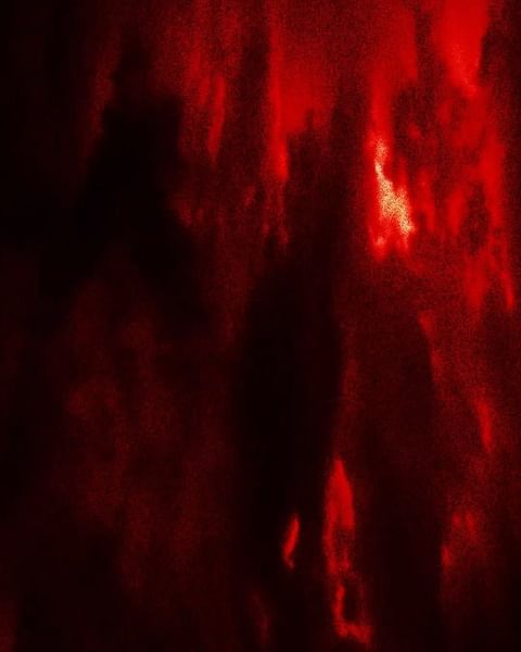 Abstract blurred background with red and black color gradients and shadowy figures blending into the dark, textured backdrop.
