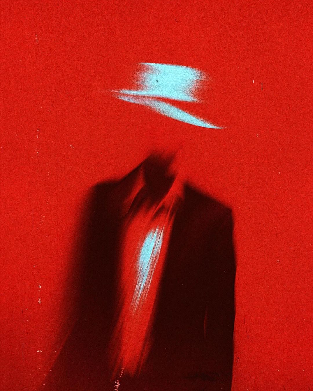 Abstract image of a person in a suit and hat with motion blur against a solid red background, creating a dynamic and mysterious effect.