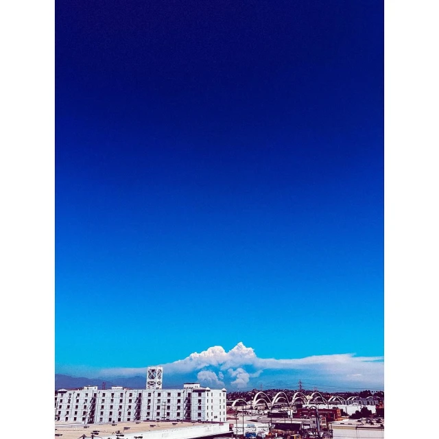 Downtown Los Angeles cityscape under a vast blue sky, featuring modern white buildings and a distant bridge silhouette on the horizon.