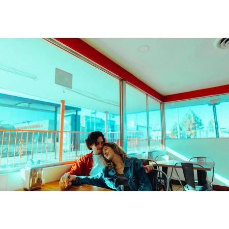 Couple in casual attire sitting at a table in a vintage diner with natural window light creating a cozy, intimate atmosphere. 