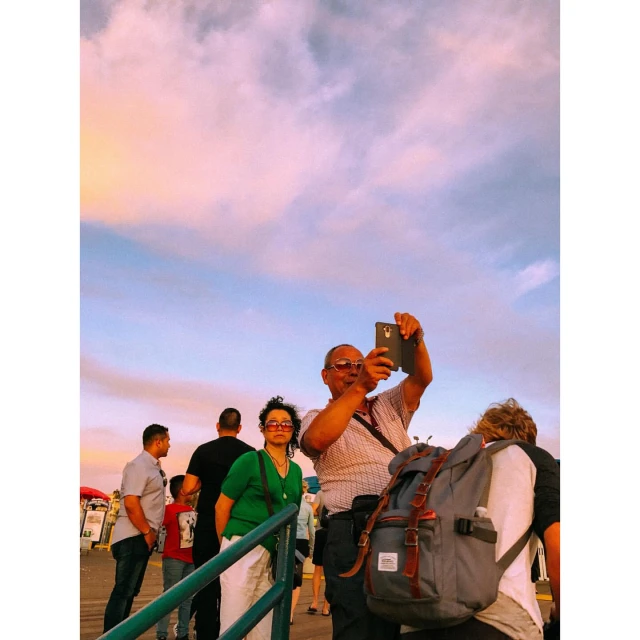 Outdoor shot of an elderly man taking a photo with his smartphone on a pier as a woman in a green sweater stands near him.