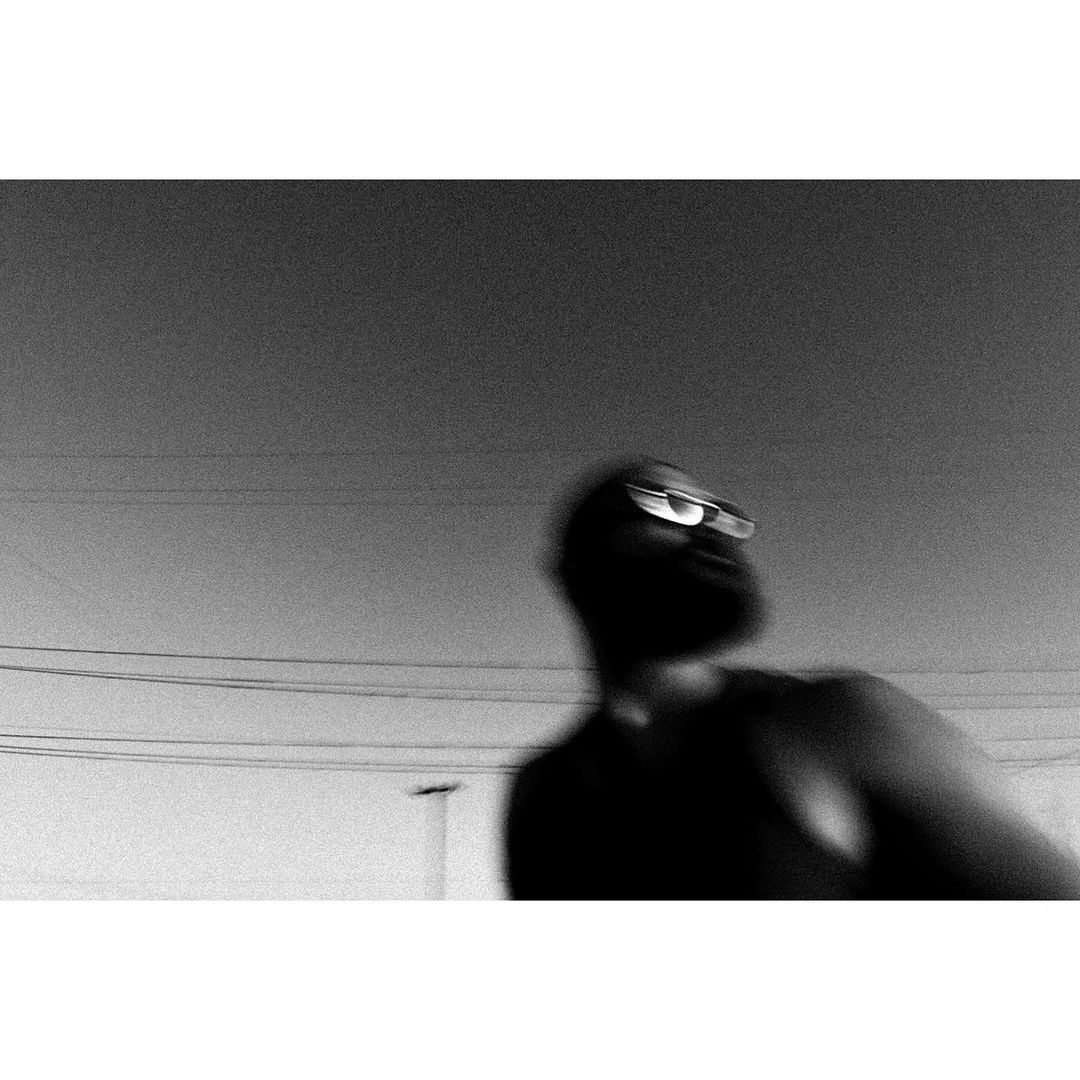 Motion blurred black and white photograph of a bearded man wearing glasses against an empty sky