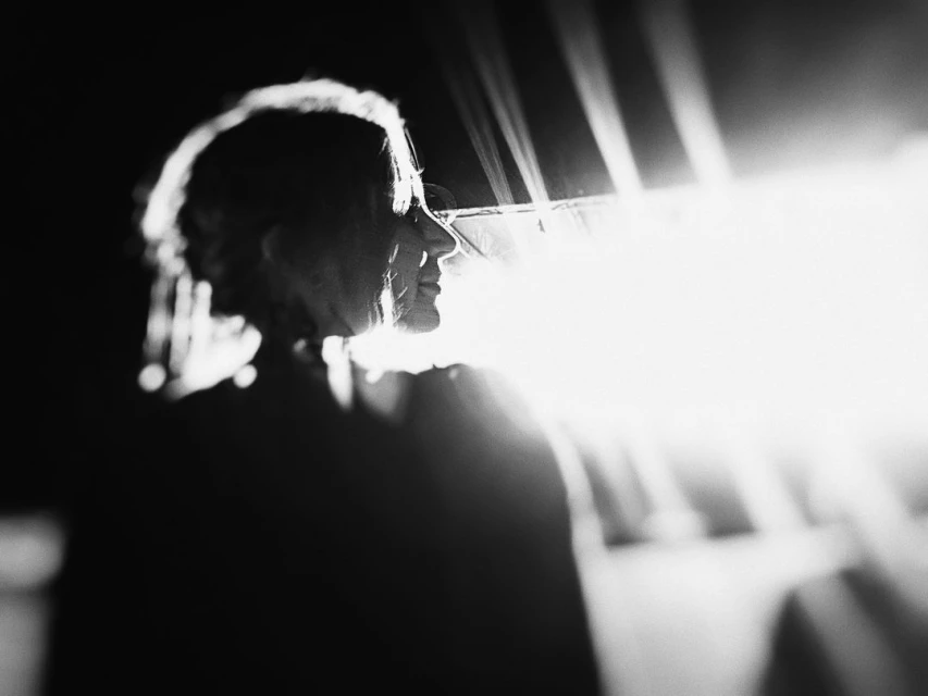 Monochrome portrait of a woman in profile, lit by backlight, shows her silhouette and the subtle textures of her hair and facial features.