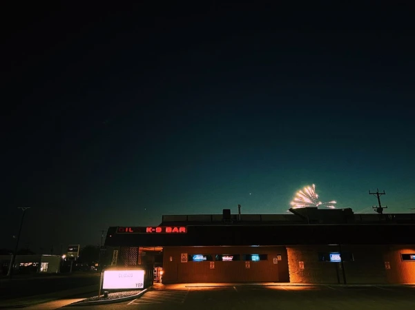 Night scene of Gil K-9 Bar under a dark blue sky with a burst of fireworks in the distance and a closed sign out front.