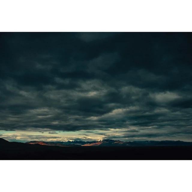 Scenic landscape with dramatic cloudy sky over distant mountains, creating a moody and atmospheric vista.