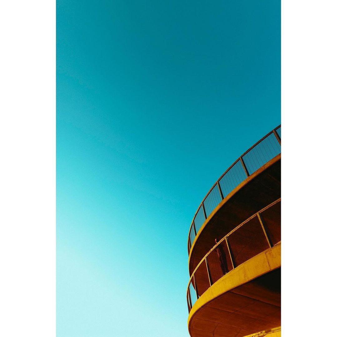 Low-angle architectural view featuring a curved building structure against a clear blue sky. Minimalist composition with vibrant color contrast.