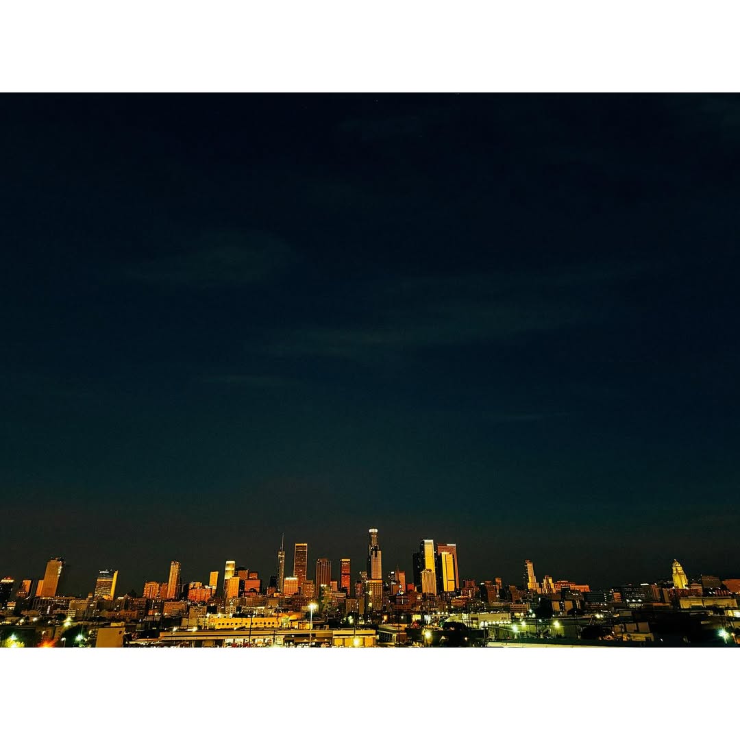 Night cityscape view of Los Angeles, California, featuring illuminated skyline and urban landscape under dark blue sky.