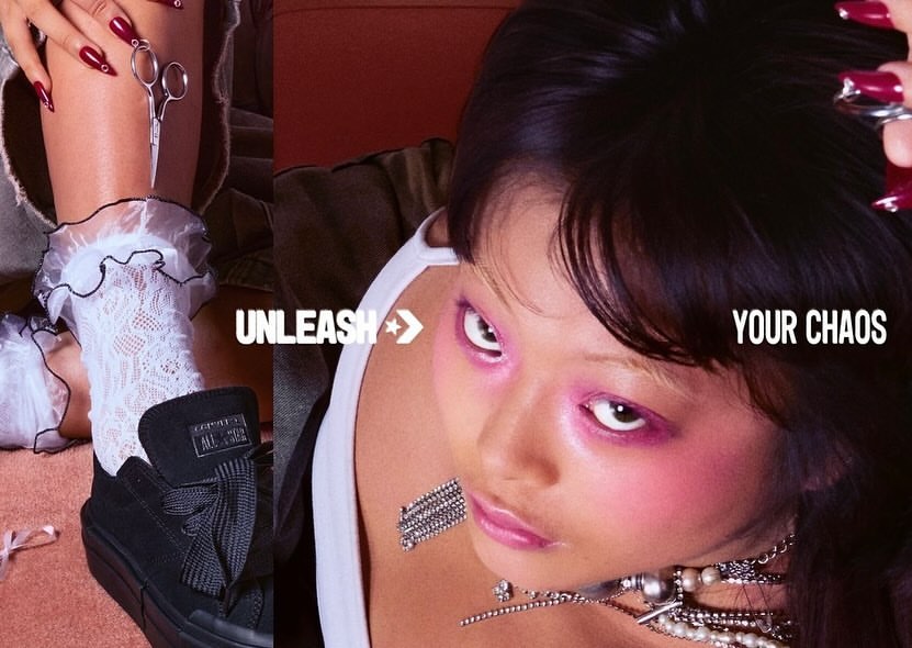 Eye-level shot of a stylish woman with bold makeup, wearing jewelry, with a Converse shoe in the foreground, in a fashion-forward aesthetic.