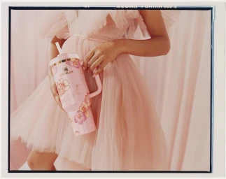 Woman in pink ruffled dress holding a floral patterned pink tumbler cup against a soft curtained backdrop