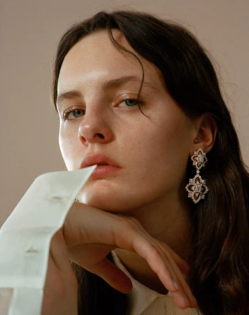 Close up portrait of a young woman resting her chin on her hand, wearing ornate diamond drop earrings and a white shirt