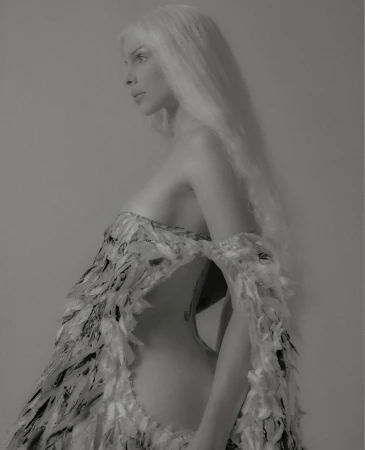 Elegant woman in a high-fashion sculptural dress made of feathers poses in profile against a neutral background, showcasing textures and design.