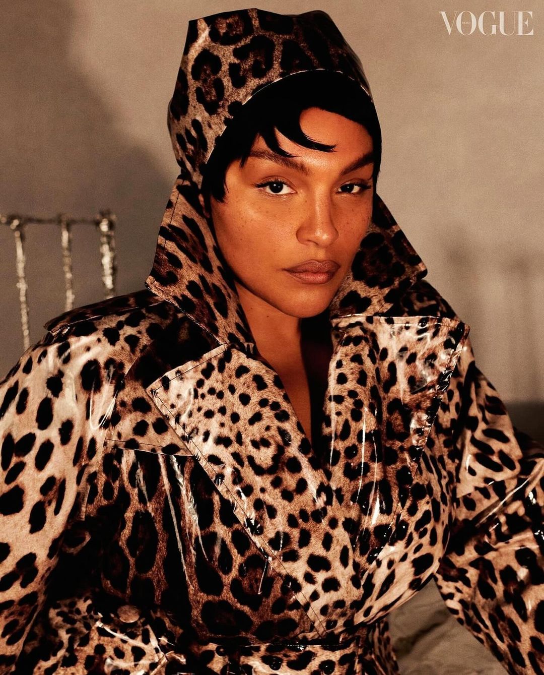 Close-up of a woman wearing a leopard print coat and head covering looking at the camera; Vogue logo in upper right corner.