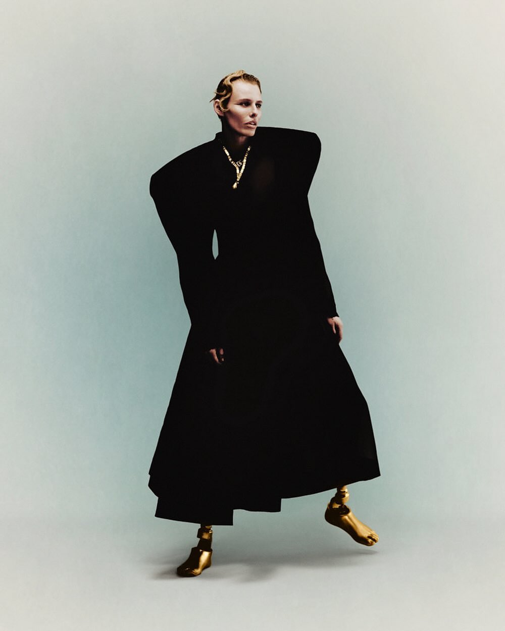 Fashionable adult woman in black sculptural coat poses in a studio with golden legs. Conceptual fashion photography. Studio shot.