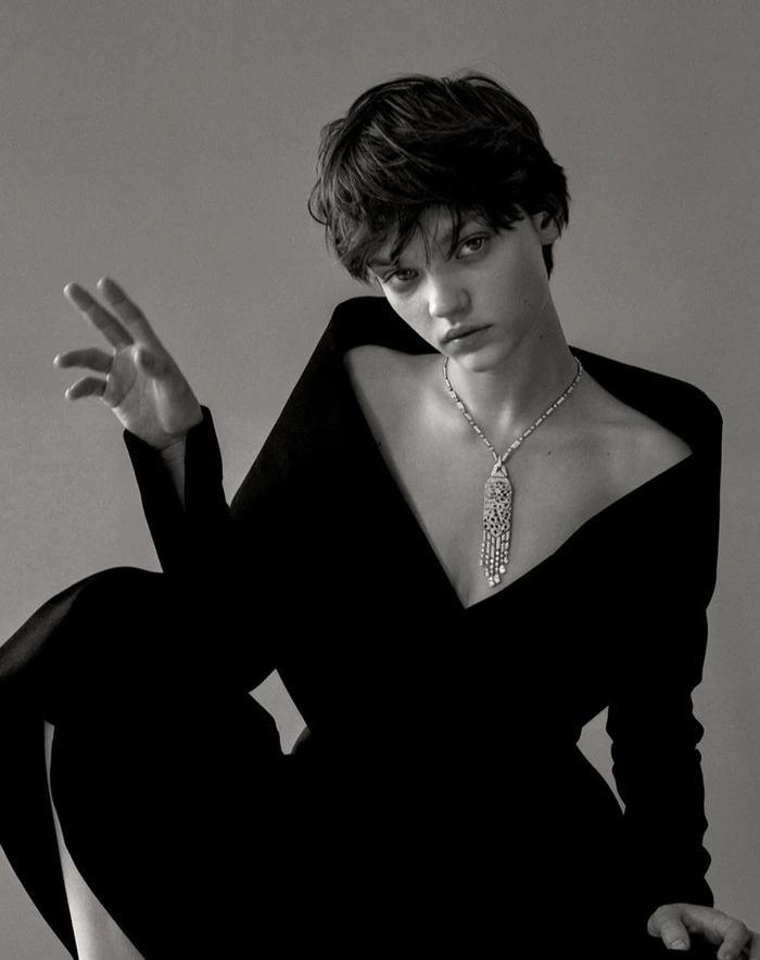 Monochrome portrait of a short-haired model wearing a dark v-neck top and a long pendant necklace by Zee Nunes