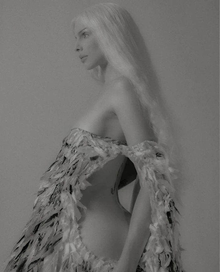 Profile portrait of a white woman with long light hair wearing an ornate textured off-the-shoulder garment