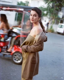 A woman in a strapless dress and draped jacket looks back over her shoulder on a city street.