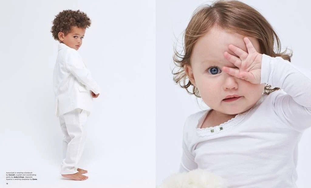 Two young children in an indoor studio setting. The child on the left wears a white suit, while the child on the right wears a white top.