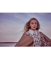 Young girl wearing a patterned shirt with a white collar outdoors near water under a dusky sky, photographed by Zoe Adlersberg.