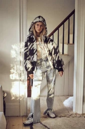 Woman in black and white houndstooth zip-up hoodie and flared jeans standing indoors near a staircase.