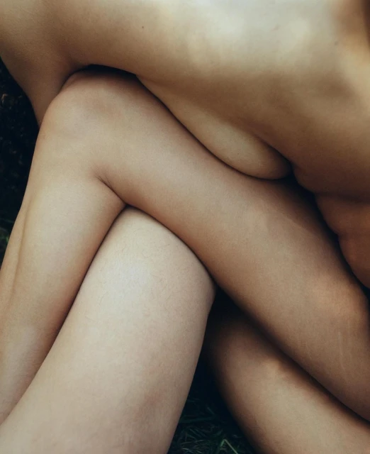 Close-up of intertwined human legs and torsos with varied skin tones against a dark green leafy background, showcasing intimacy.