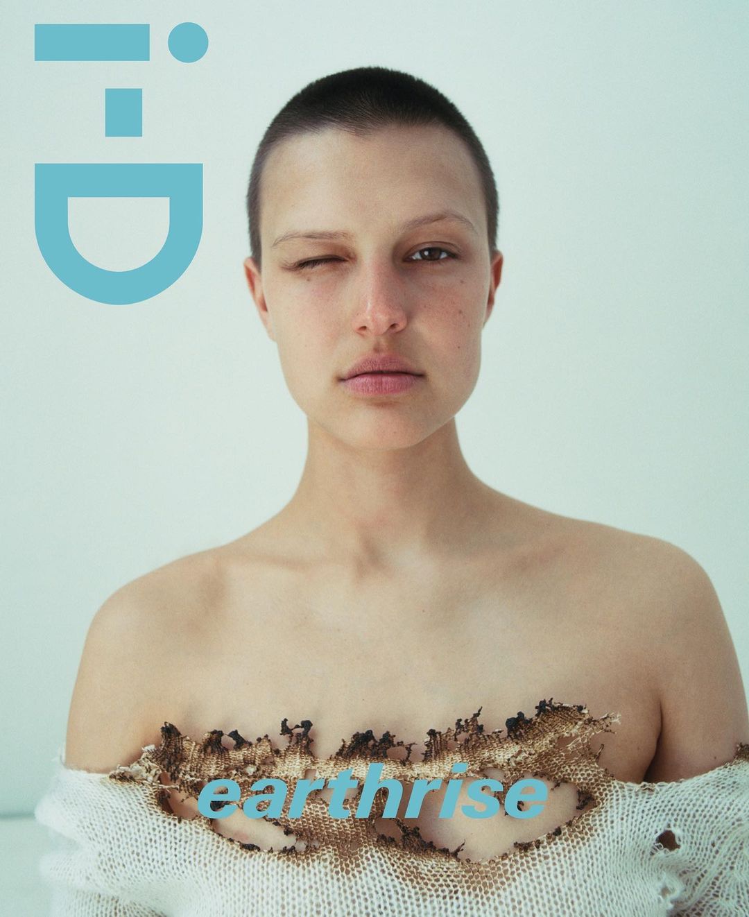 Magazine cover featuring a portrait of a woman with a shaved head, wearing a ripped sweater, set against a white backdrop.