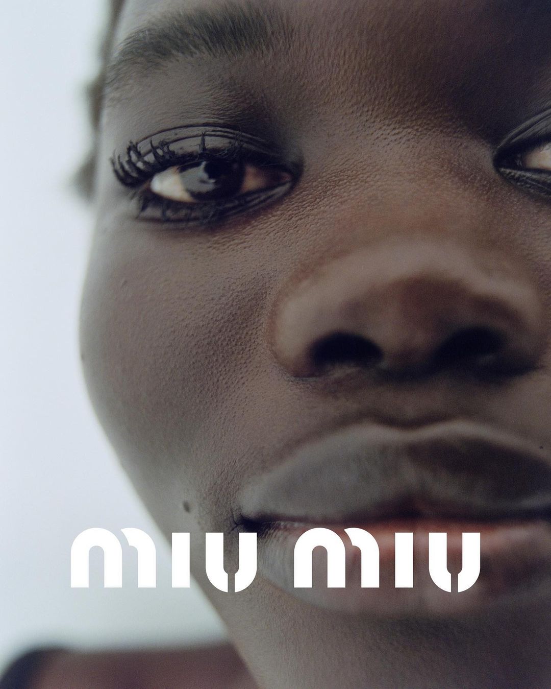 Close-up portrait of a Black woman with sleek skin and dark eyes, featuring a logo at the bottom. Focus on beauty and fashion.