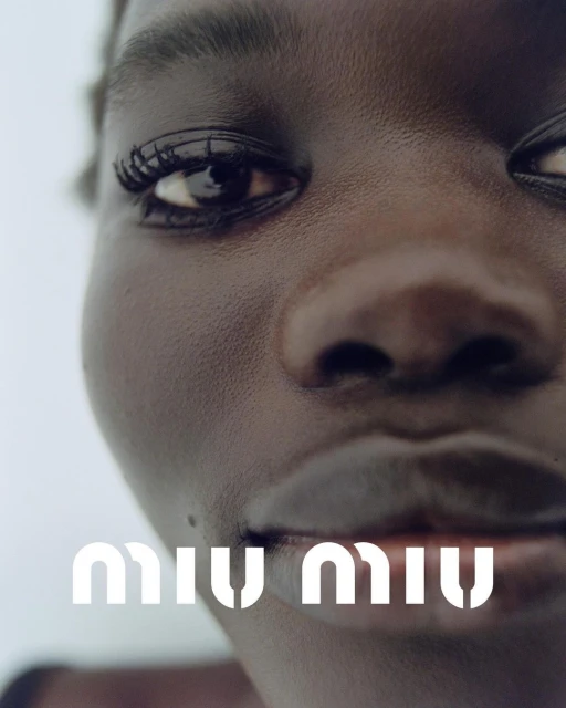 Close-up portrait of a Black woman with sleek skin and dark eyes, featuring a logo at the bottom. Focus on beauty and fashion.