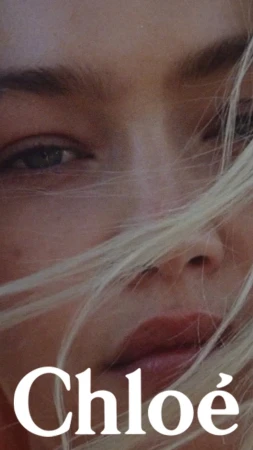Close-up portrait of a woman with blonde hair blowing across her face and white Chloe text overlaid at the bottom.