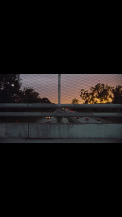 View of a highway with multiple cars visible through a chainlink fence with a colorful sunset in the background at dusk.