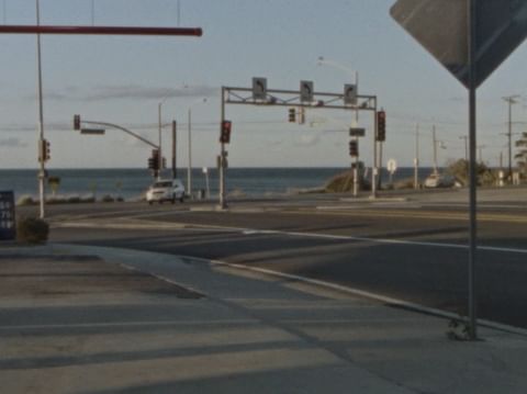 A coastal road scene at an intersection with traffic lights, a glimpse of the ocean in the background, and clear daytime lighting.