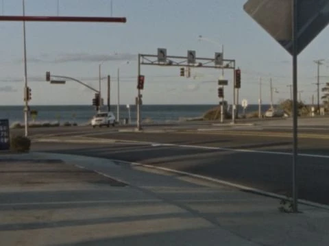 A coastal road scene at an intersection with traffic lights, a glimpse of the ocean in the background, and clear daytime lighting.