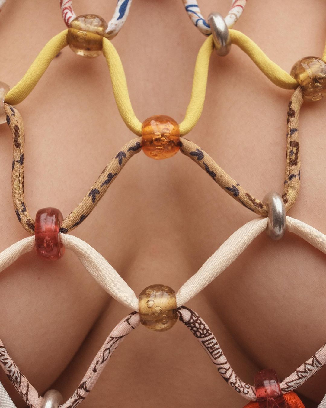 Close-up of a person wearing a handmade beaded top. The top features a net-like design with colorful beads and patterned fabric strips.