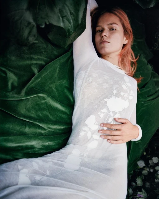 Woman with pink hair in white dress reclines in botanical setting with large green leaves. Fashion and beauty portrait in nature.