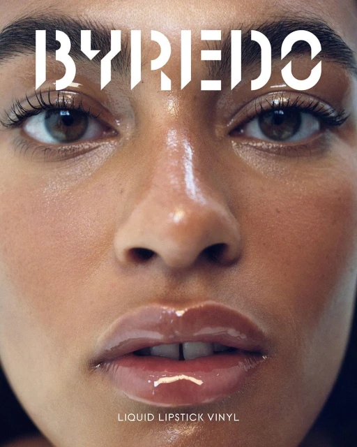Close-up shot of a woman's face with brown eyes and glossy lips, featuring the 'BYREDO' logo above her face and 'LIQUID LIPSTICK VINYL' below.
