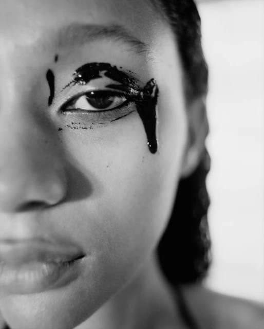 Monochrome close-up portrait of a woman's face with black paint around her eye, creating a dramatic and artistic effect.