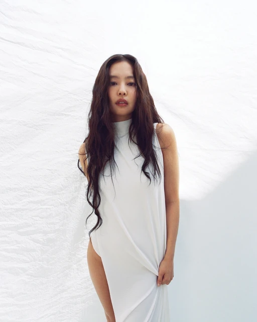 Portrait of a woman with long dark hair wearing a white dress standing in front of a white fabric backdrop in a photo studio.