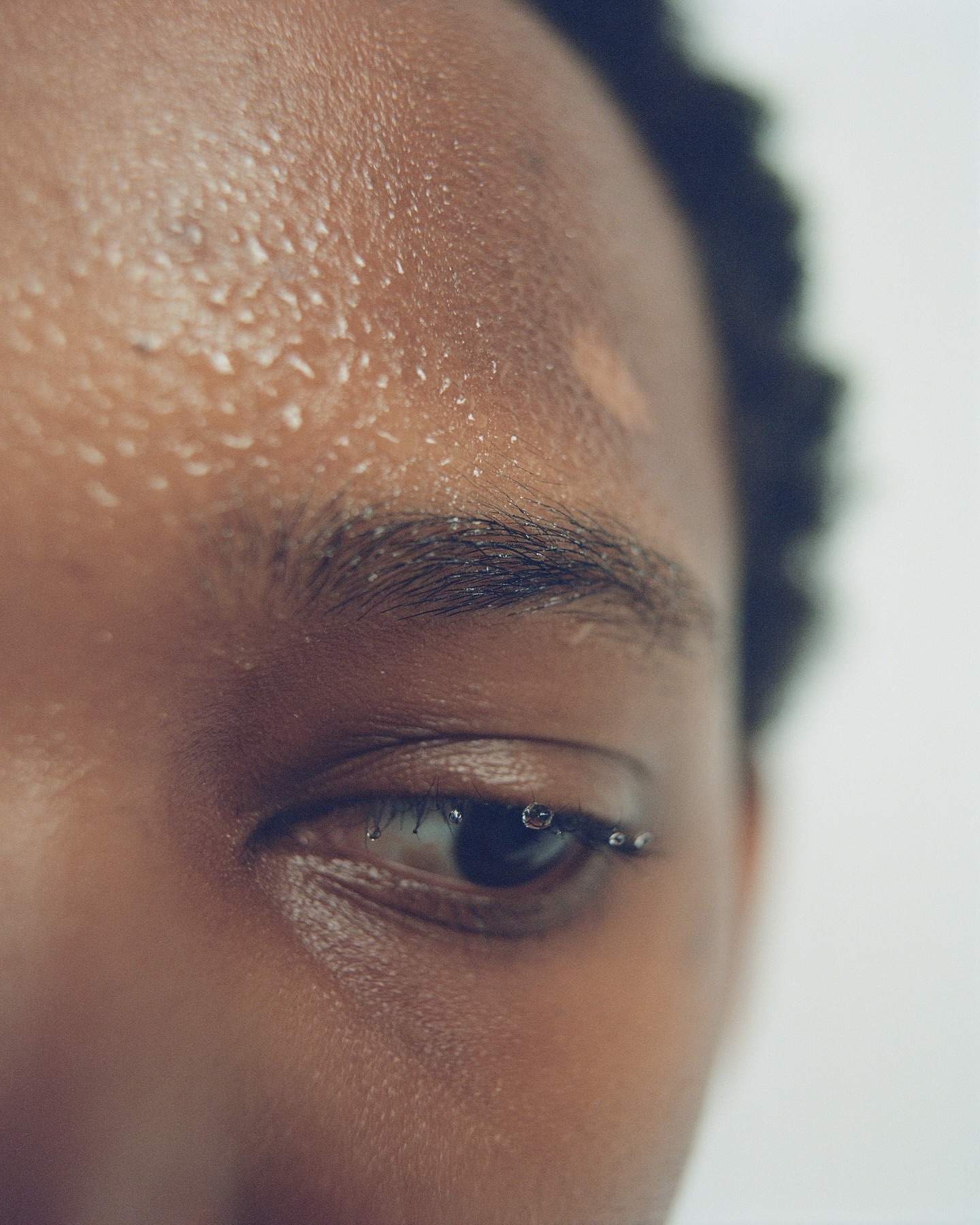 Close-up of an adult woman's face showing skin with water droplets and her eye with a row of water droplets on the eyelashes.