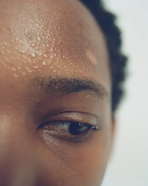 Close-up of an adult woman's face showing skin with water droplets and her eye with a row of water droplets on the eyelashes.