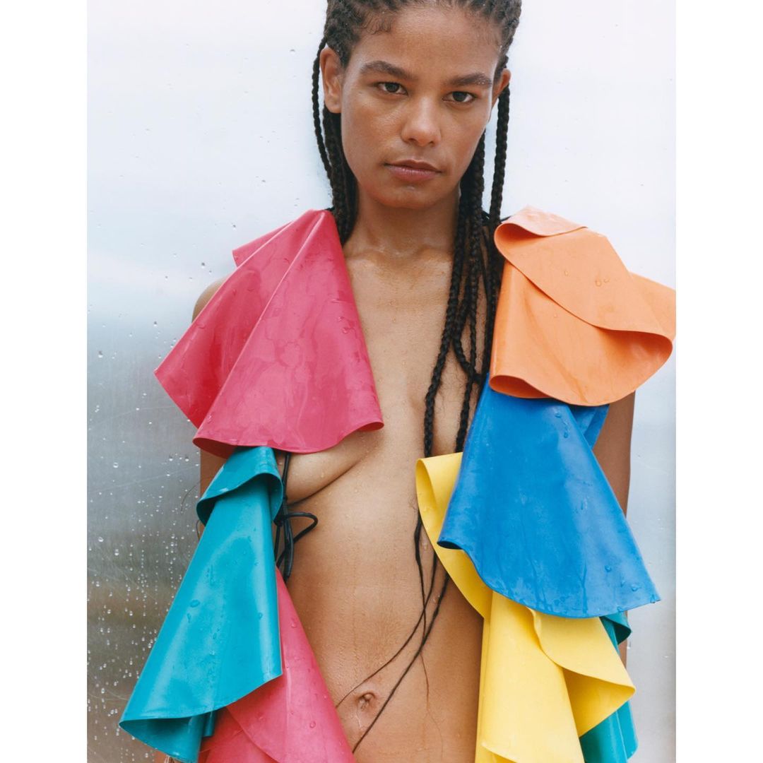 Portrait of a model with colorful, layered vinyl ruffles against a white and grey backdrop, styled with black braided hair.