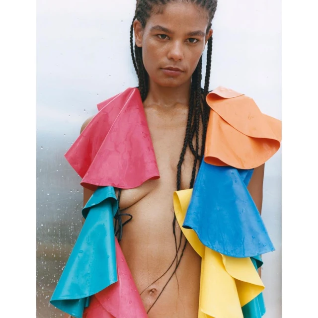 Portrait of a model with colorful, layered vinyl ruffles against a white and grey backdrop, styled with black braided hair.
