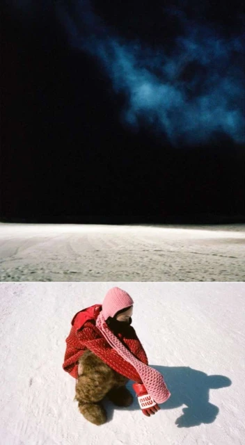 Child in a red jacket sits on snow, hugging a teddy bear against a dark night sky and snow-covered ground. Knitted pink scarf and hat visible.